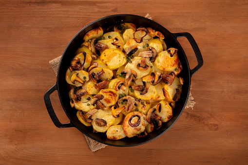 A photo of a dutch oven with cooked vegetables, potato, green peas, mushrooms, shot from the top on a dark rustic background with a place for text, a vegan meal