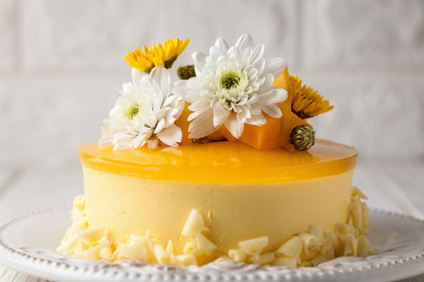 istock Glazed Mango cheesecake with white and yellow flowers and fresh mango pieces on grey background, horizontal composition 1075285758