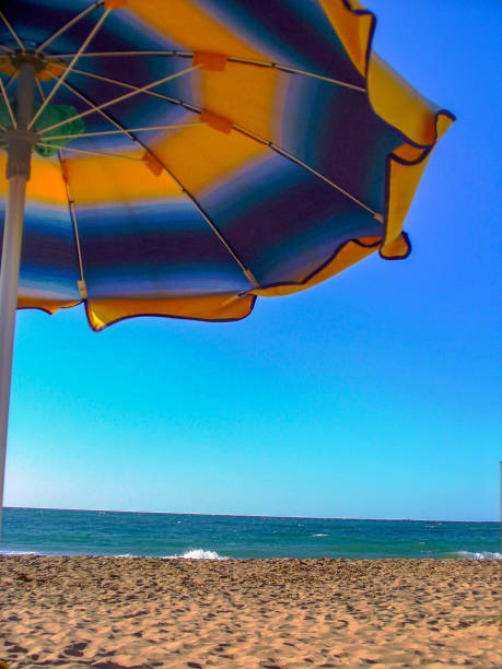 multicolored umbrella on a sandy beach with sea and horizon on background, in sicily, trapani province