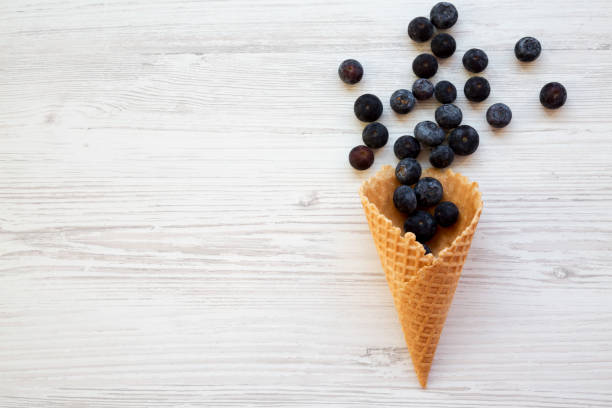istock Waffle sweet ice cream cone with blueberries on a white wooden table, top view. Flat lay, overhead, from above. Space for text. 1075368814