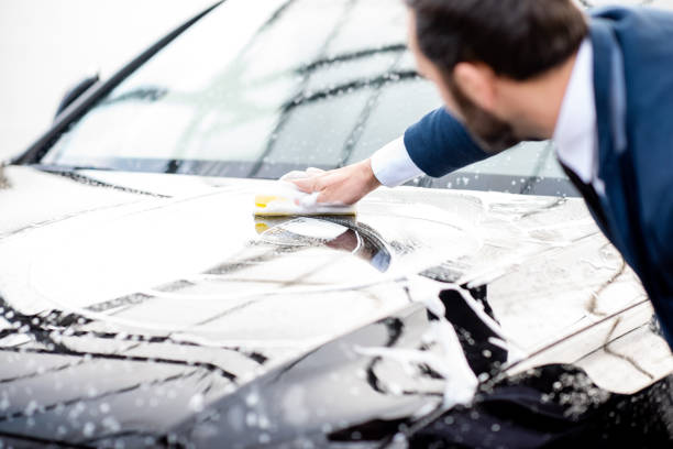 Elegant businessman dressed in the suit washing his car with yellow sponge and foam on a self service car wash