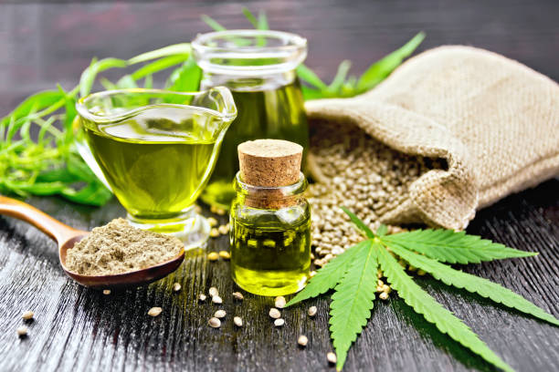 Oil hemp in two jars and sauceboat on wooden board Hemp oil in two glass jars and sauceboat with grain in the bag, leaves and stalks of cannabis, a spoon with flour on the background of wooden boards cannabaceae stock pictures, royalty-free photos & images