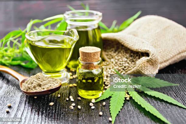 Oil Hemp In Two Jars And Sauceboat On Wooden Board Stock Photo - Download Image Now - Cannabis Plant, Hemp, Cooking Oil