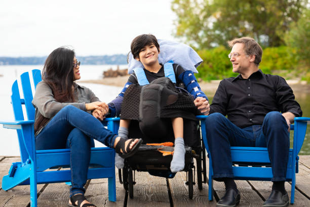 Multiracial couple with disabled boy in wheelchair outdoors by lake stock photo