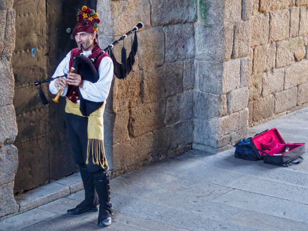 Santiago de Compostela, Galicia, Spain - October 3, 2014: Camino pilgrims are welcome by a Galician bagpipes player busking under a stone archway (Arco de Palacio) leading to the Obradoiro Square