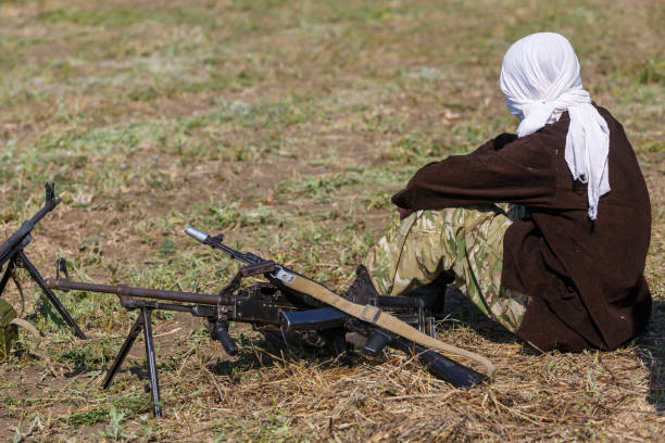 white veiled soldier sits on the ground close to a machine gun - jihad imagens e fotografias de stock