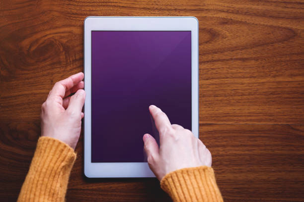 istock Digital Tablet Mockup Image. Screen as Clipping Path. Woman Touching on a Display, Wooden Table, Top View 1075397532
