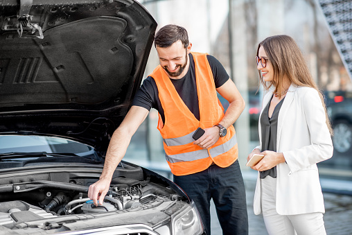 Handsome service worker consulting or providing technical assistance of the broken car to the businesswoman outdoors