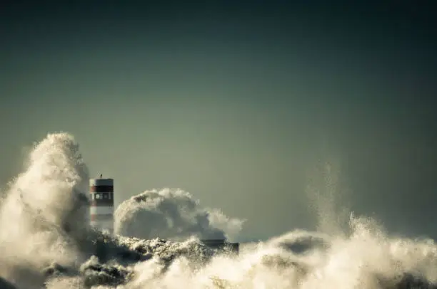 Photo of lighthouse with a big wave of water from the ocean with blu sky