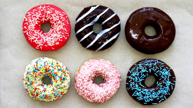 Donuts of different colors on cardboard, top view, stop motion animation. Full HD