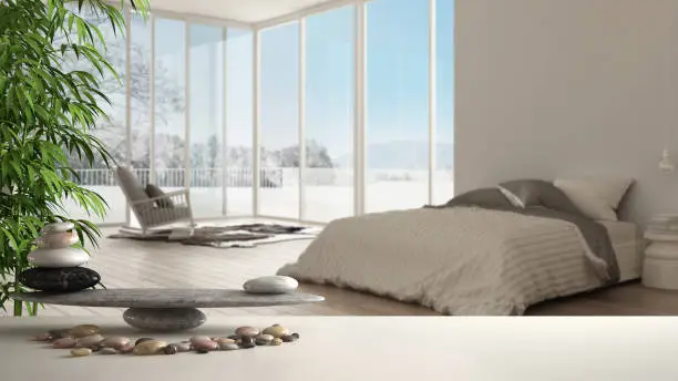 Wooden vintage table or shelf with stone balance, over blurred minimalist bedroom with big panoramic window, carpet and armchair, feng shui, zen concept architecture interior design