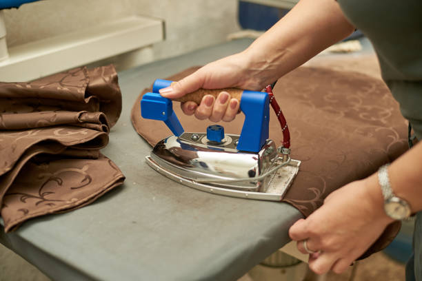 istock Woman stroking a brown material with an iron on an Ironing Board. 1075429946