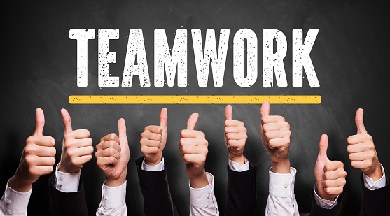 many thumbs up in front of a blackboard with the word teamwork