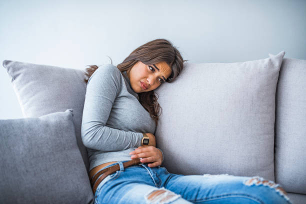 mujer joven en dolor acostado en el sofá en casa - belly ache fotografías e imágenes de stock