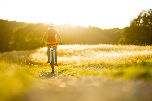 warm summer sunlight back light rural landscape grassland sportive woman cycling electric mountain bike trail