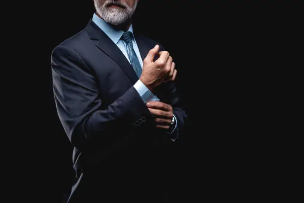 elegant mature fashion man looking at his cufflinks while fixing them