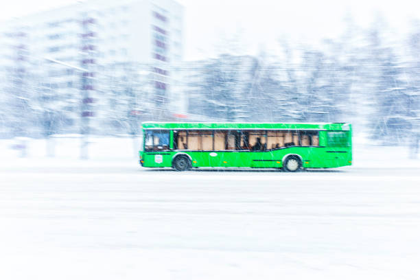 Green city bus rides a snowbound road during a snow storm. Abstract blur background. Concept of dangerous road conditions in winter
