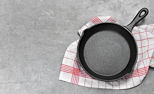 Cast iron pan on a grunge concrete background with copy space. Empty iron pan, top view or high angle shot.