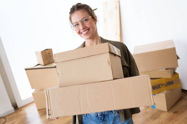 istock Pretty young woman carrying cardboard boxes into her new house while smiling at camera. 1075501408