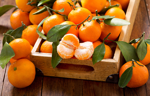 plate of fresh tangerines, oranges, mandarins, or clementines with leaves on wooden table. still life. close up.
