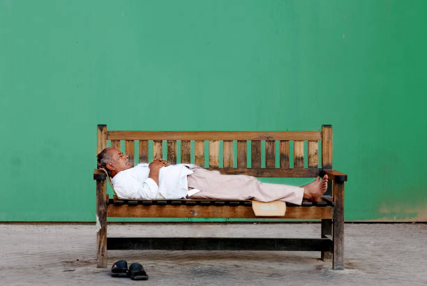 OLD TOWN, DUBAI, UAE - AUGUST 2009: Poor old homeless Indian man sleeping on a wooden bench in front of a green wall. Editorial use only.