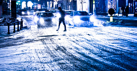 Blurry snowy city night traffic with pedestrian silhouette crossing the street