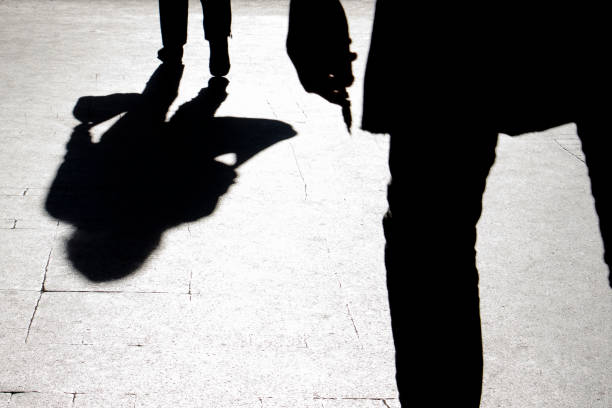 Blurry silhouette and shadow of a woman carrying a bag and a man holding sharp object following her stock photo