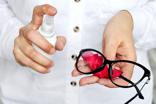 Women hand  holding white spray bottle cleaning trendy black glasses lens with red microfiber tissue.healthcare, vision and medicine concept