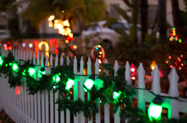 Southern CA Christmas lights, garlands, and candy canes on a white picket fence at dusk.