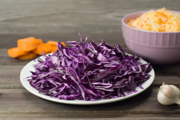 Photo of Photo of the salad of purple cabbage close-up and sauerkraut with carrots in a plate on a dark wooden background.
