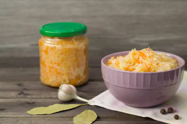 Photo of Sauerkraut in a plate and sauerkraut in a jar on a dark wooden background.