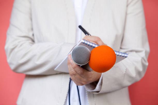 istock Female journalist at news conference, writing notes, holding microphone 1075559462