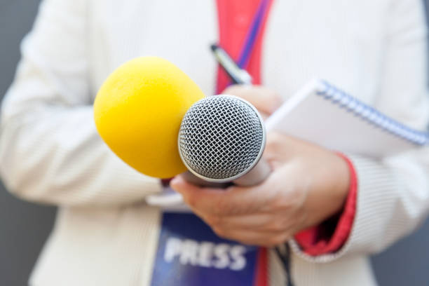 Female journalist at news conference, writing notes, holding microphone