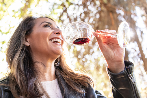 Smiling hispanic or middle eastern mature woman drinking wine