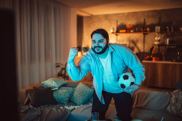 istock Fat man watching football at home 1075587830