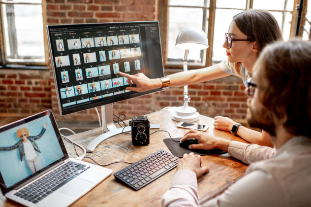 Couple of photographers working on computers in the studio Young couple of photographers working with woman's portraits at the working place with two computers in the studio photo editing screen stock pictures, royalty-free photos & images