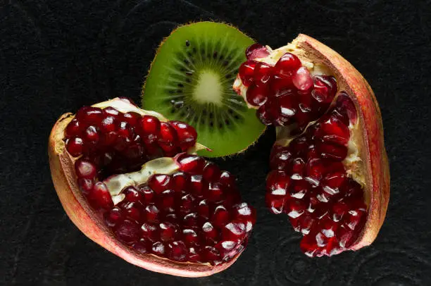 Photo of Ripe and juicy pomegranate and kiwi fruit close-up on a black background.