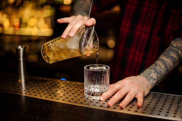 istock Barman pouring strong alcohol into a cocktail glass with ice cube using strainer 1075639940