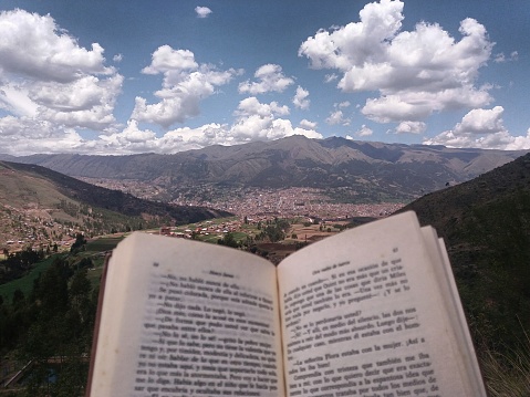 very close open book with background of mountains with trees and distant city, cloudy sky background, location, san jeronimo, cusco, peru.