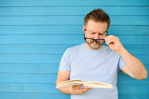 Retrato de hombre maduro con gran negro gafas tratando de leer el libro pero tiene dificultades viendo texto debido a problemas de visión photo