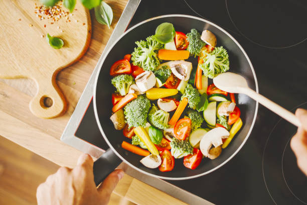 uomo che cucina verdure fresche in padella - healthy eating food vegetable fungus foto e immagini stock