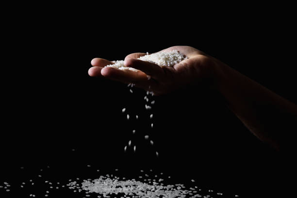 istock Rice falling through the fingers of male hand. Dark background 1075663152