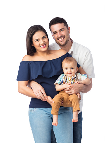 A lovely latin family of three with a baby boy, standing and smiling at the camera.