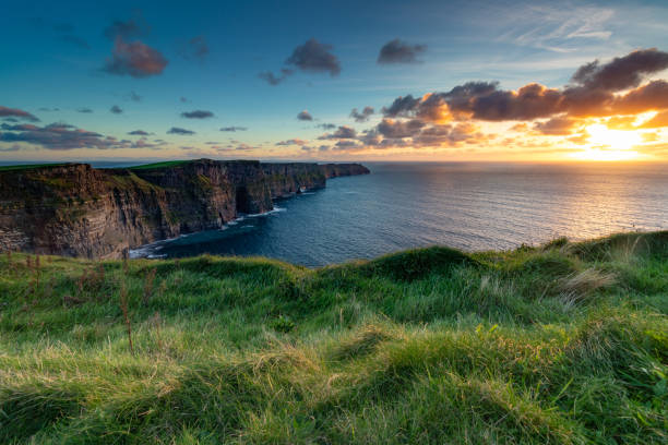 Cliffs of Moher at Sunset Overlooking ocean on a cliff with grass in foreground. bluff stock pictures, royalty-free photos & images