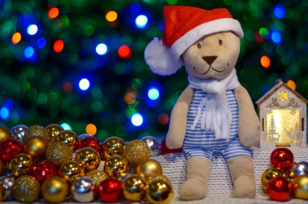 istock Teddy bear wearing hat and scarf sitting between Christmas baubles and ornaments with colorful bokeh lights as background for Christmas Holiday. 1075777628