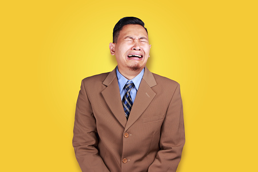 Portrait of funny Asian businessman crying hard against orange background