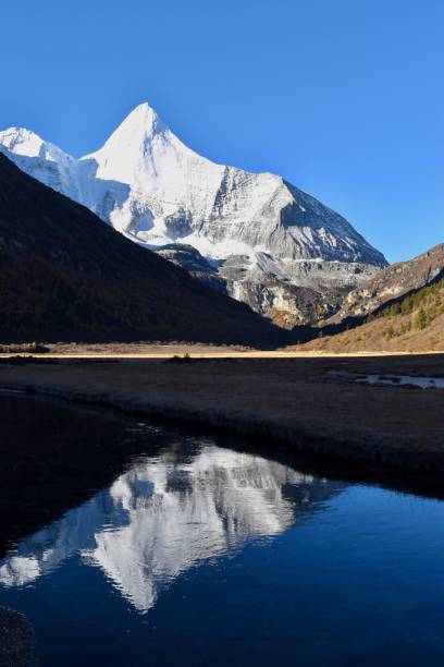 istock Sacred mountain Jambeyang (5,958m) with blue sky background and its reflection on icy clean lake. This place is supposed to be the real Shangrila. Daocheng Yading Nature Reserve, Sichuan, China. 1075885178
