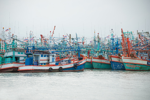 Thai Fishing Boats, colorful greens and blues and oranges. Docked with grey sky.