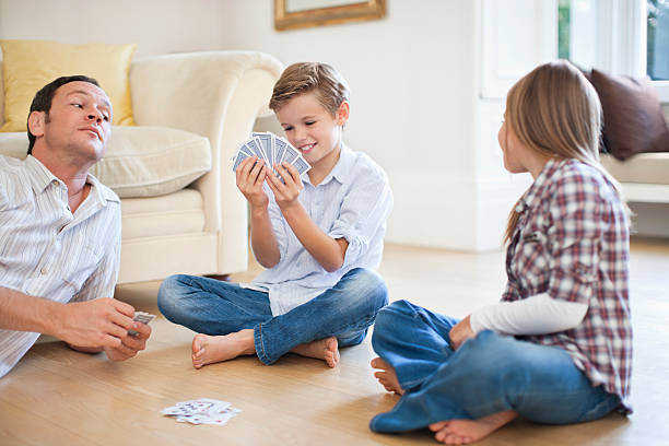 Father and daughter (8-9} peeping into boy's (10-11) cards  family playing card game stock pictures, royalty-free photos & images