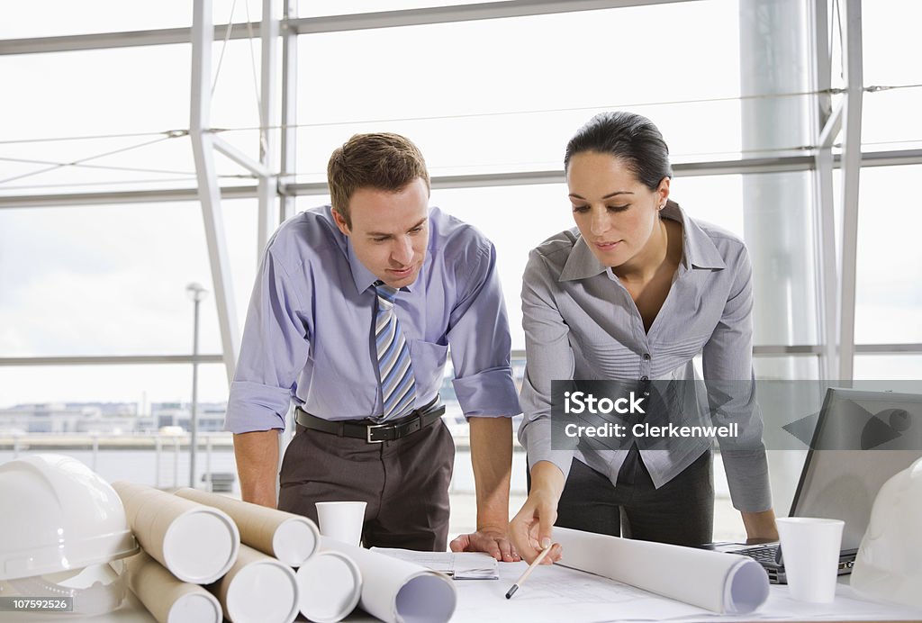 Dos arquitectos trabajando en azul imprime en el escritorio de oficina - Foto de stock de 25-29 años libre de derechos